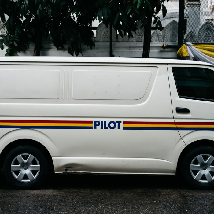A parked white van with 'PILOT' branding, seen in an urban environment.