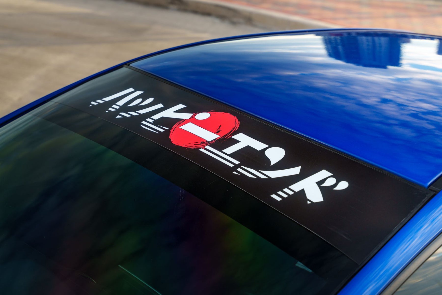 Close-up of a car's windshield with a Japanese-themed decal on a sunny day.