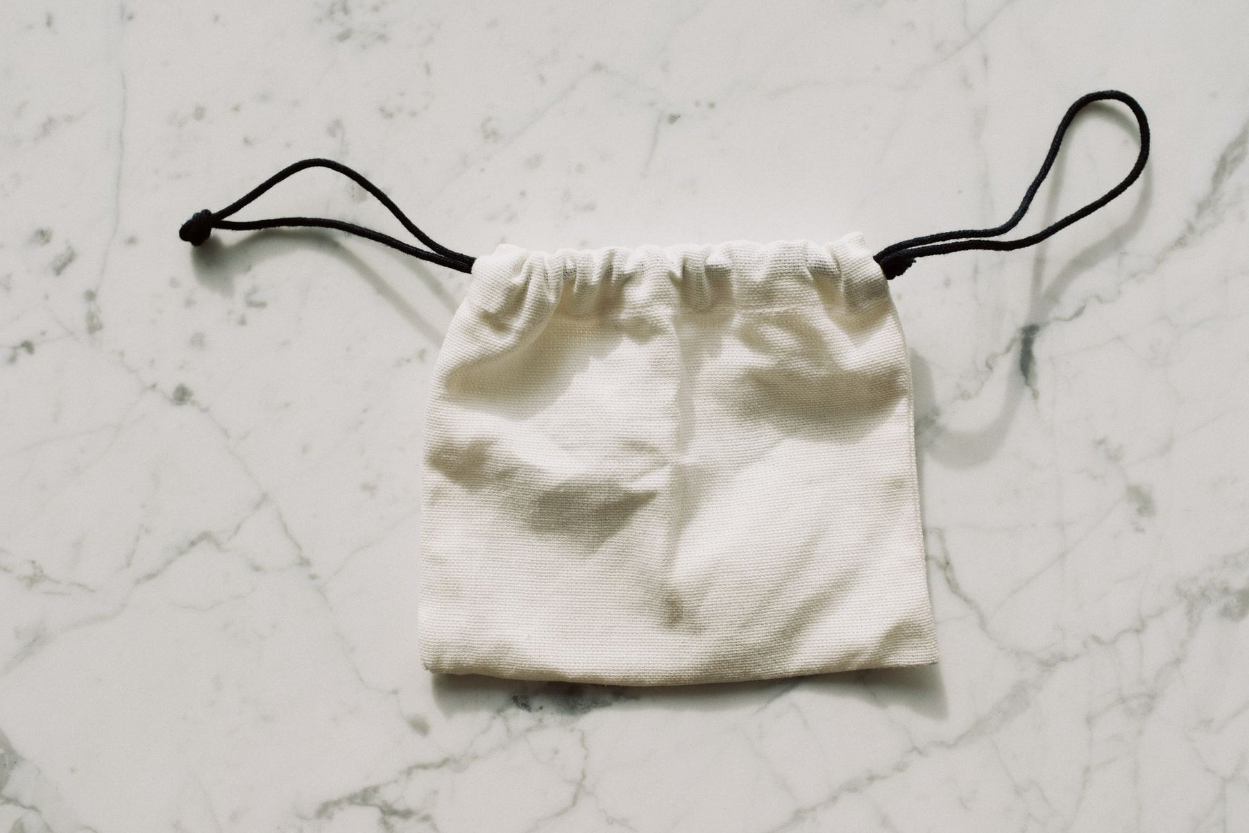 A simple white drawstring pouch on a marble surface, perfect for storing small items.