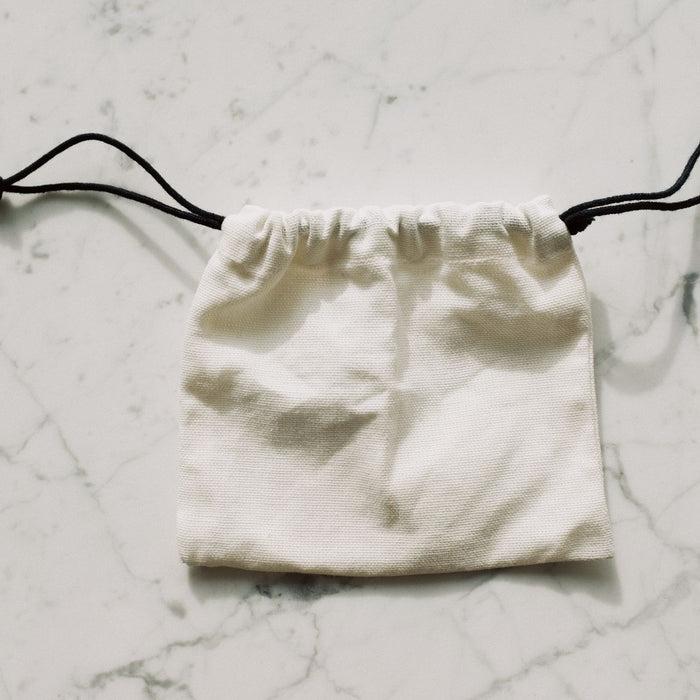A simple white drawstring pouch on a marble surface, perfect for storing small items.