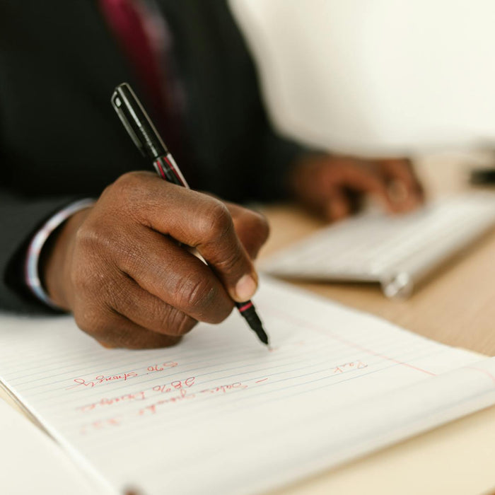 Close-up of a businessman writing notes in a notepad at a desk, highlighting stationary and productivity.