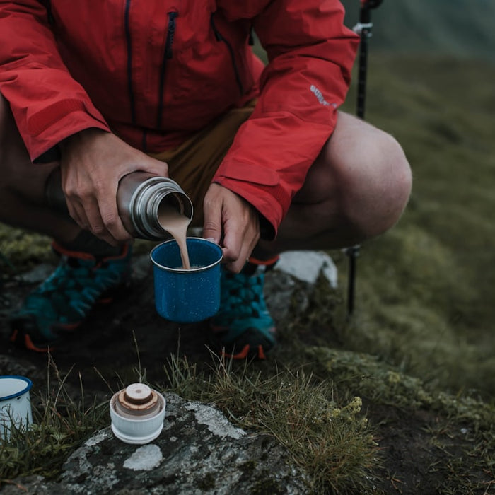 man pouring brown liquid on blue cup
