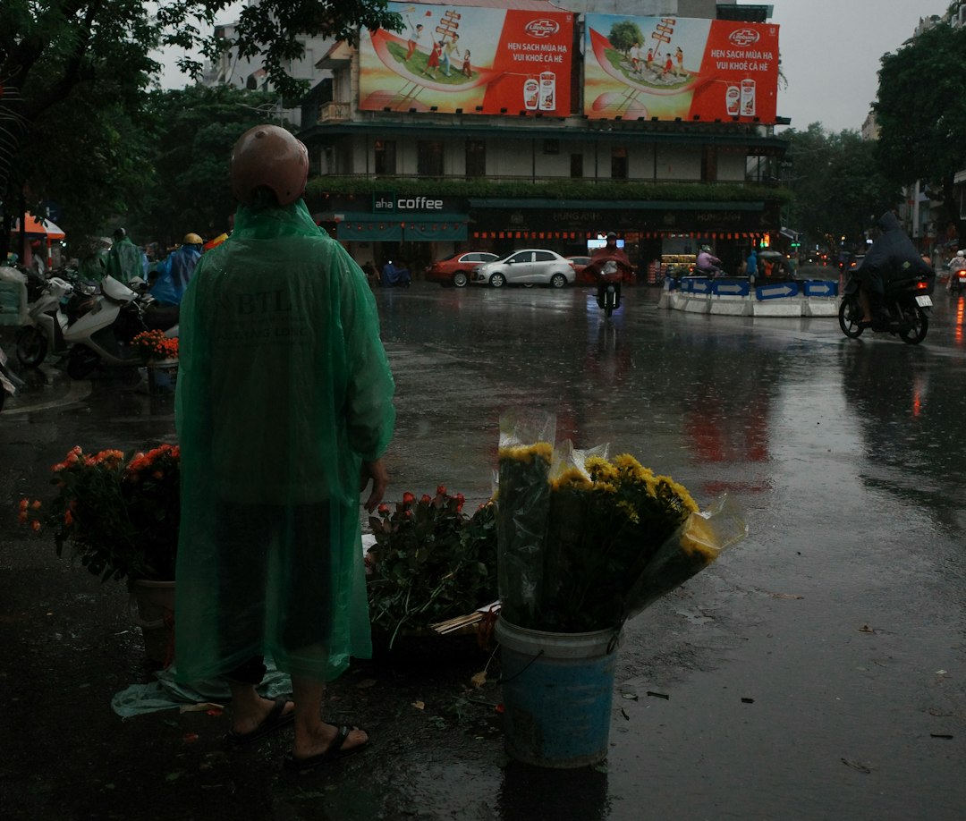 Person in green raincoat stands by flower stall in rain