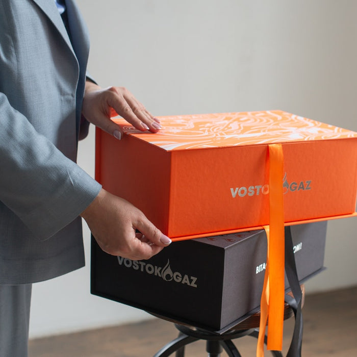 Hands opening a bright orange gift box with ribbon