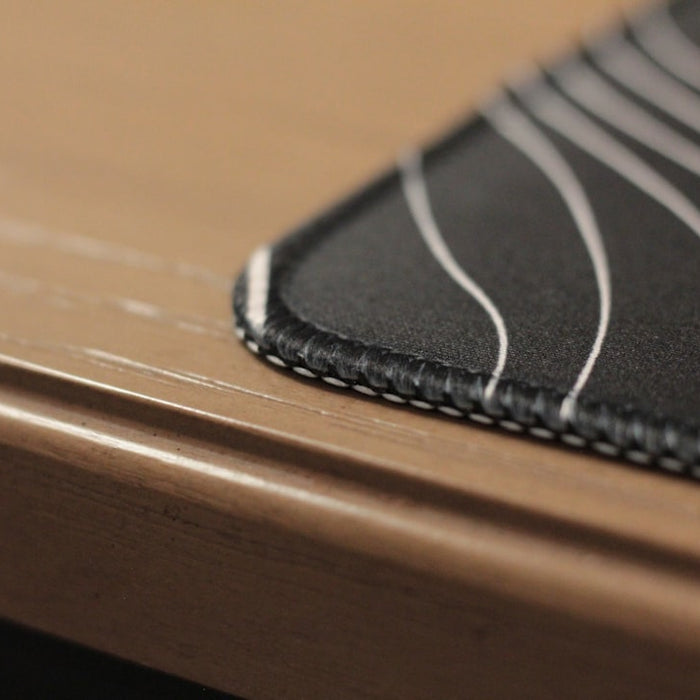 Close-up of a black mousepad on a wooden desk.