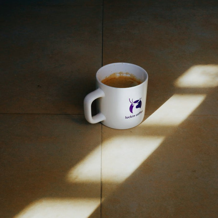 A white mug filled with coffee sits on a floor