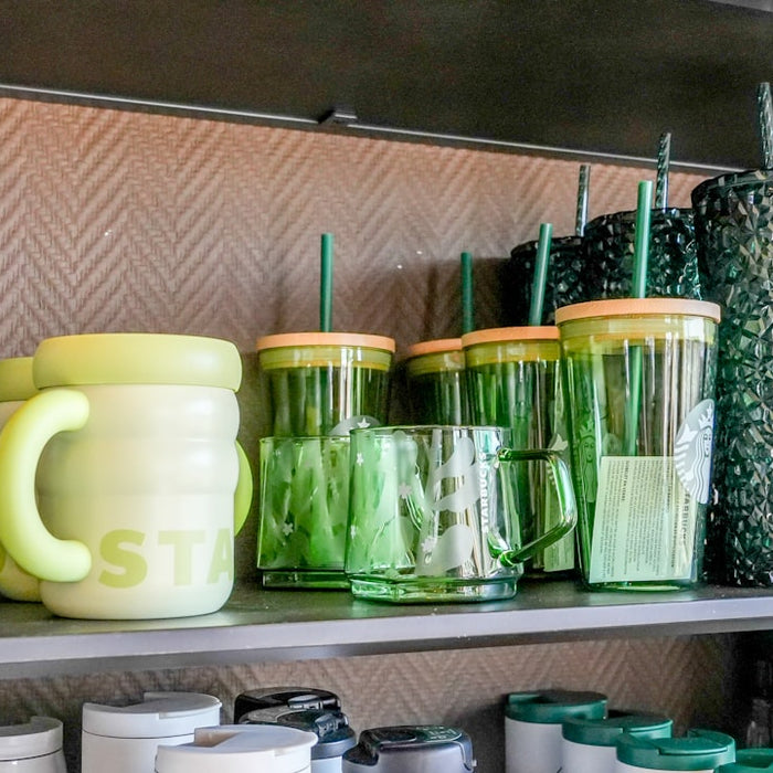 Green and yellow mugs and tumblers displayed on a shelf.