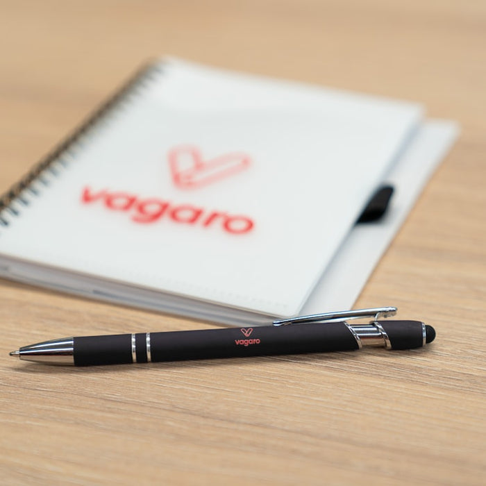Pen and notebook with vagaro logo on a wooden surface.
