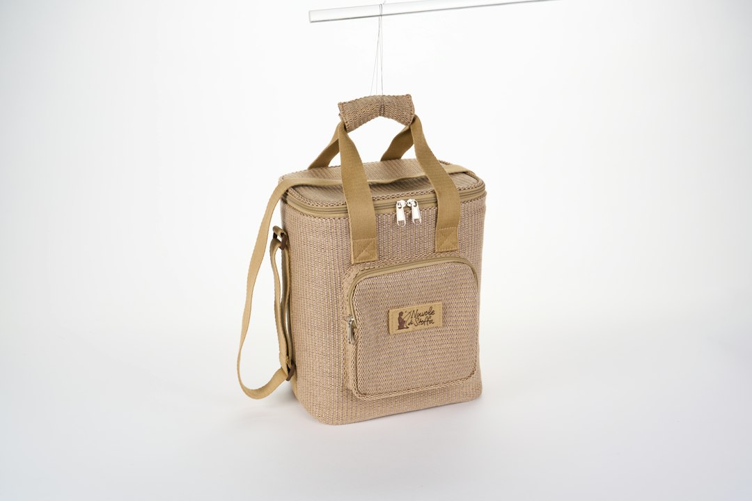 A beige woven cooler bag with a shoulder strap hanging against a white background