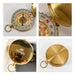 Luminous Compass - A gold compass with a decorative face, featuring a logo on the glossy surface and a ring for attachment.