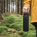 350ML/500ML Double Wall Stainless Steel Drink Bottle with Handle - A drink bottle in matte black, featuring a handle, held by a person in a yellow jacket amidst a forested background.