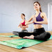 Mantra Yoga Mat - A yoga mat in green with floral patterns, used by two women seated in a meditative pose on a wooden floor.