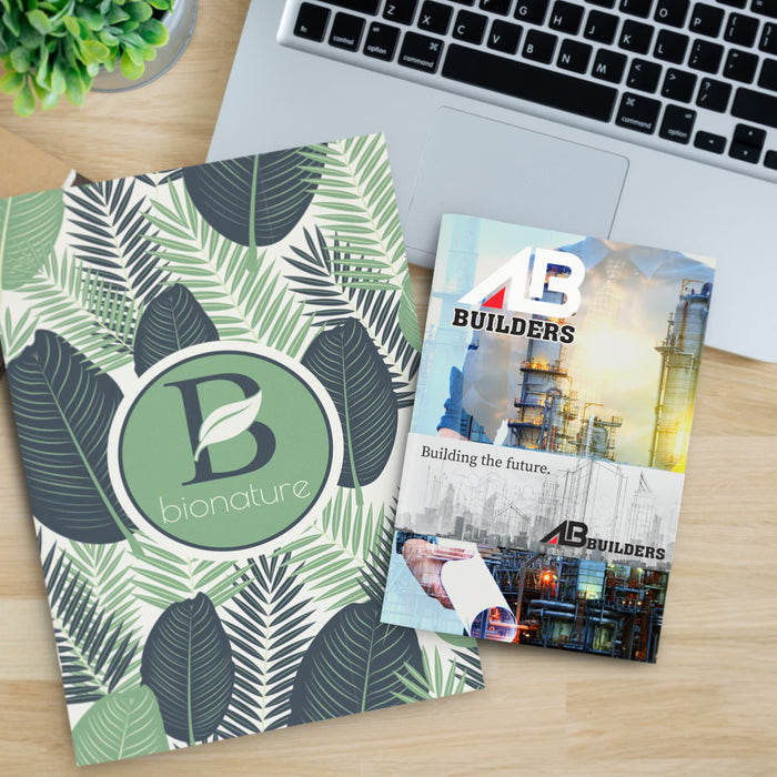 Camri Full Colour Notebook - Medium - A medium notebook with a green leaf design alongside a brochure on a desk with a laptop and a plant.