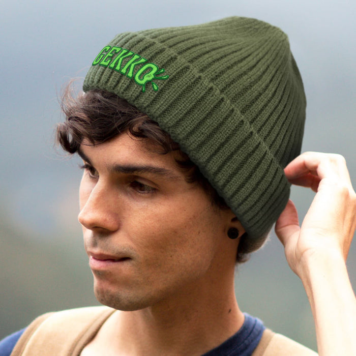 Denali Beanie - An olive green ribbed beanie with a logo, worn by a person with curly hair.