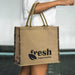 Modena Jute Tote Bag - A jute tote bag in natural brown with dark patterned sides and a logo on one side.