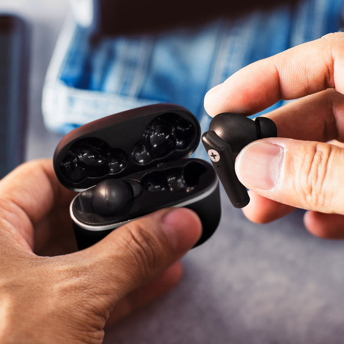 Swiss Peak TWS Earbuds 2.0 - A pair of black earbuds are held above their charging case, with a casual background of denim fabric.