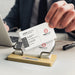 Bamboo Business Card Stand - A bamboo business card stand holds several white business cards with black text, alongside a smartphone and a notebook.