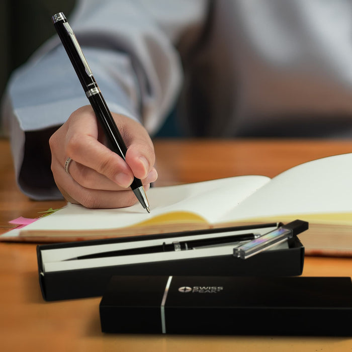 Swiss Peak Luzern Pen and Pencil Set - A black pen and pencil set in a sleek box, with a hand writing in a notebook. The set includes a branded logo.