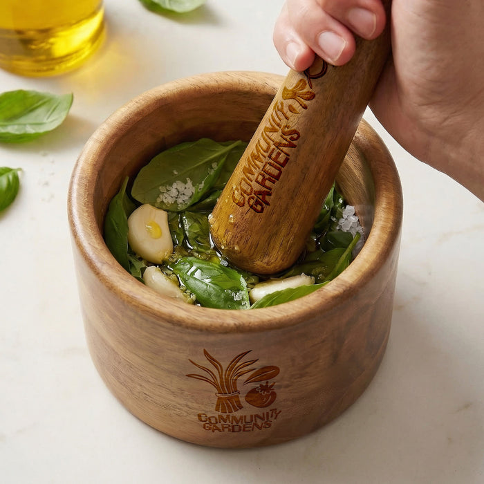Keepsake Mortar & Pestle - A wooden mortar and pestle filled with fresh basil, garlic, salt, and oil, featuring a logo on the side.