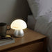 Portobello Table Lamp - A table lamp with a soft, white dome shade and a silver base, placed on a wooden bedside table with a coffee cup and glasses.