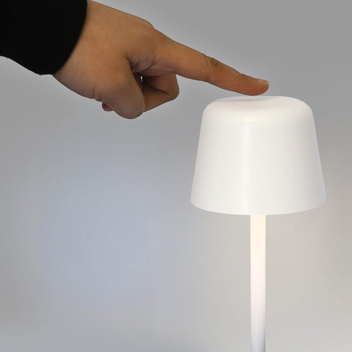 Ember Rechargeable Table Lamp - A white rechargeable table lamp with a tapered design, being turned on by a hand pressing the top.