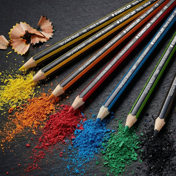 Staedtler Colouring Pencil Set of 6 - A set of six coloured pencils in yellow, orange, red, blue, black, and green, with shavings and colour powder scattered around.