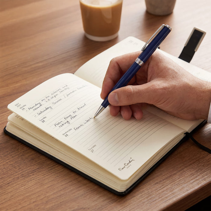 Pierre Cardin Fontaine Weekly Diary - 2027 - A diary with cream-coloured pages and a pen resting on a wooden table, alongside a coffee cup.