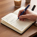 Pierre Cardin Fontaine Weekly Diary - 2027 - A diary with cream-coloured pages and a pen resting on a wooden table, alongside a coffee cup.
