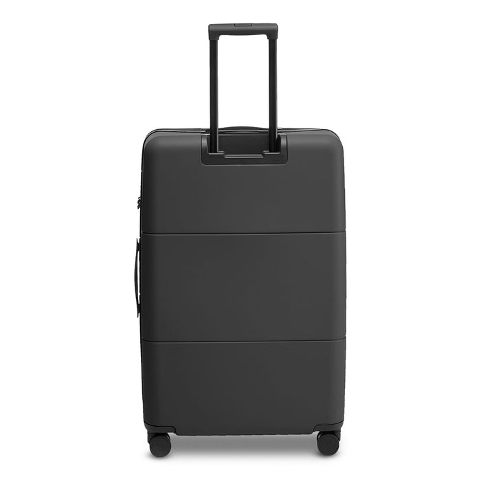 Kadi Check-In Suitcase - Large - A large black suitcase with a retractable handle and wheels, featuring a smooth surface and an attached logo.