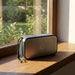 Swiss Peak 10W Bass Speaker - A grey Bluetooth speaker sits on a windowsill, showcasing a sleek design with a logo on its front.
