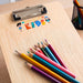 Prism Print - 90 x 25mm Sticker - A wooden clipboard with a colourful logo and a set of vibrant coloured pencils arranged beside it.