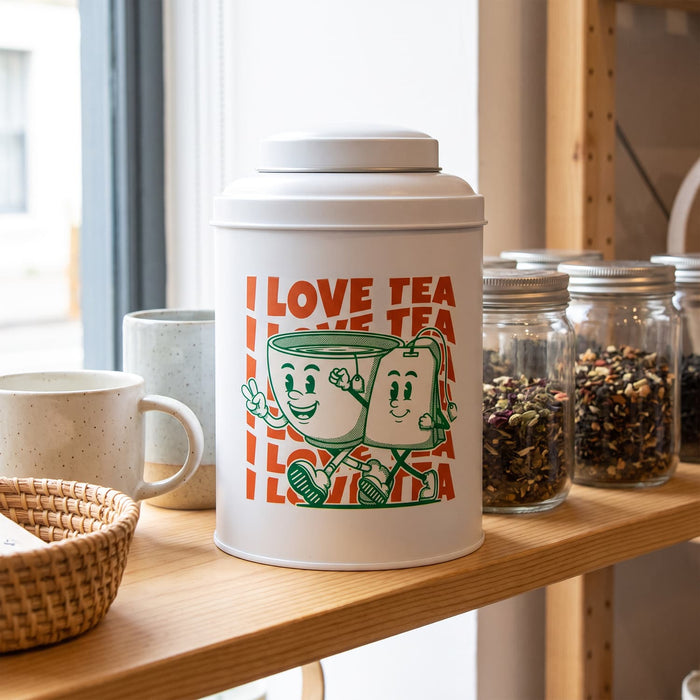 Prism Print - 100 x 100mm Sticker - A white tea canister with green illustrations of two cheerful mugs, displayed on a wooden shelf alongside jars and cups.