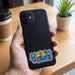 Prism Print - 60 x 40mm Sticker - A hand holds a black phone with a colourful "Good Vibes" sticker on its back, placed on a wooden table.