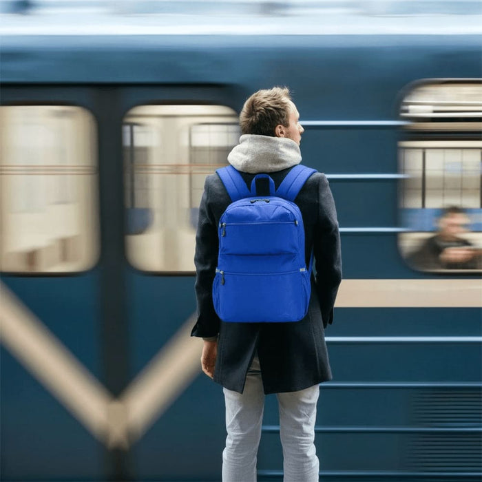 High Sierra Everclass Backpack 24L - A man stands at a train station wearing a blue High Sierra Everclass Backpack. The background features a blurred train.