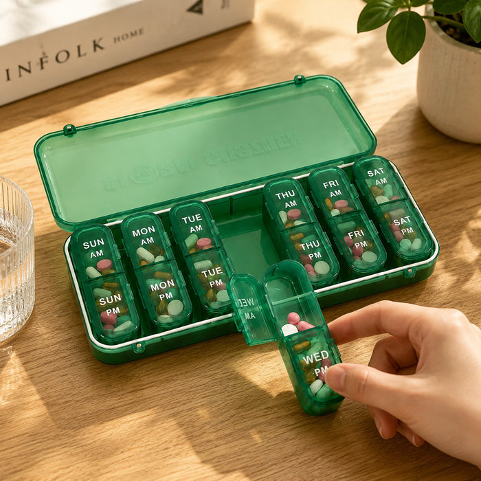 7 Day Pills Organizer - A green seven-day pill organiser with individual compartments for morning and evening doses, sitting on a wooden surface.