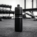 Sprint Sport Bottle 750ml - A drink bottle in black, standing upright on a gym floor with weights in the background.