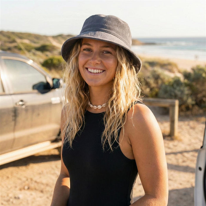 Leroy Cord Bucket Hat - A woman stands by a beach wearing a grey cord bucket hat, smiling with wavy blonde hair.