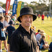 Leroy Cord Bucket Hat - A man wearing a black Leroy Cord Bucket Hat smiles at a sports field, with people and tents in the background.