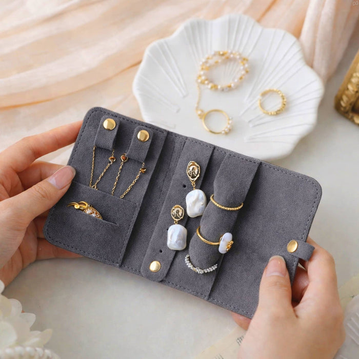 Synthetic Leather Jewellery Bag - A grey synthetic leather jewellery bag displaying various rings and earrings, held open in two hands.