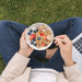 Pack of 100 Per Pack Disposable Birch Spoons/Forks (Small) - A person holding a bowl of granola topped with berries, using a small wooden disposable spoon, sitting on grass.
