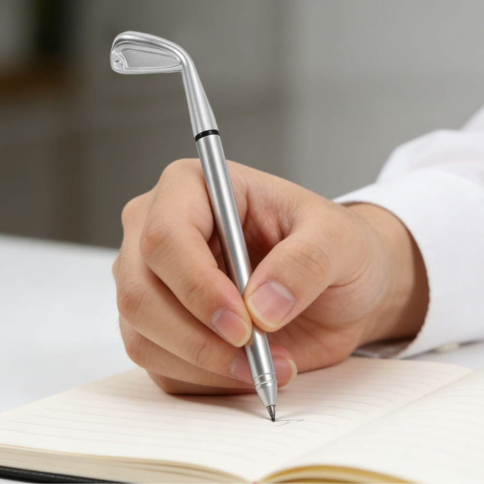 Golf Pen - A silver golf pen shaped like a golf club, held in a hand, writes on a lined notebook.