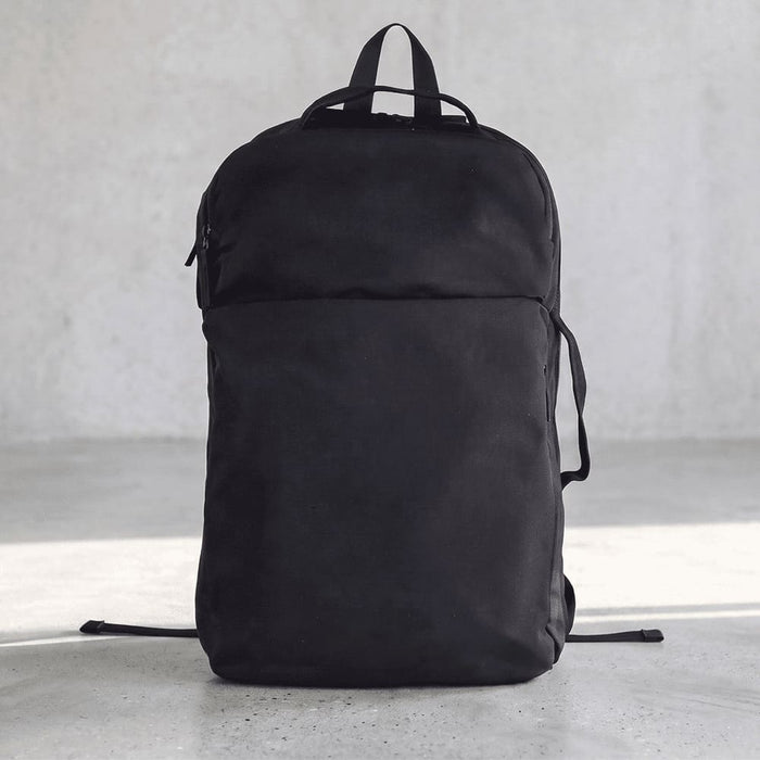 Rime Backpack - A black backpack with a sleek design and a front pocket, featuring straps and a logo on the side.