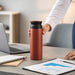 350ML/500ML Double Wall Stainless Steel Drink Bottle - A drink bottle in matte terracotta with a black lid, placed on a desk alongside a laptop and notepad.