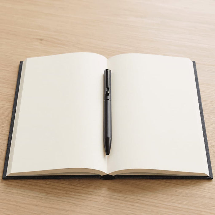 Verton Recycled Aluminium Twist Ballpoint Pen - A black ballpoint pen rests on an open, blank, black-covered notebook against a wooden background.