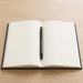 Verton Recycled Aluminium Twist Ballpoint Pen - A black ballpoint pen rests on an open, blank, black-covered notebook against a wooden background.