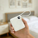 10000mAh Power Bank with Charging Cable - A white 10000mAh power bank with a charging cable and a digital display, held in a hand against a bedroom backdrop.