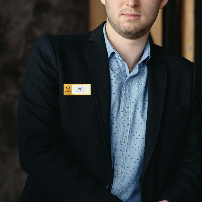 Reusable Metal Name Badge - A man in a blazer wearing a gold and silver reusable metal name badge. The background is blurred.