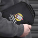 Travel Pack - A black tech case with a logo, featuring a rocket design and a handle, held by a person in a grey hoodie.