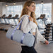 Bucket Duffle Bag With Wide Straps - A light blue bucket duffle bag with wide straps, carried by a woman in a gym setting.