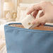 Mini Synthetic Leather Jewellery Bag - A blue synthetic leather jewellery bag with a hand placing a small cream pouch inside it.